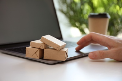 Internet shopping. Small boxes near man using laptop at table indoors, closeup