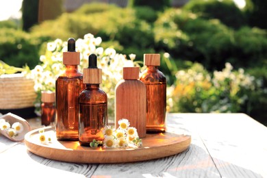 Photo of Bottles of essential oil and flowers on white wooden table outdoors, space for text