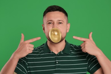 Handsome man blowing bubble gum on green background