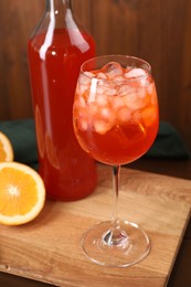 Aperol spritz cocktail and ice cubes in glass and bottle on wooden table, closeup