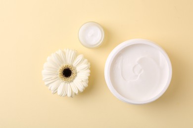 Photo of Moisturizing cream in open jars and gerbera flower on beige background, flat lay. Body care product