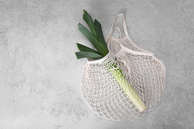 Photo of White net bag with leek on light grey table, top view