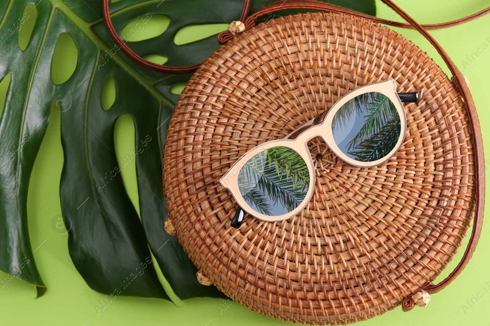 Image of Bamboo bag and sunglasses with reflection of palm trees on green background, flat lay 