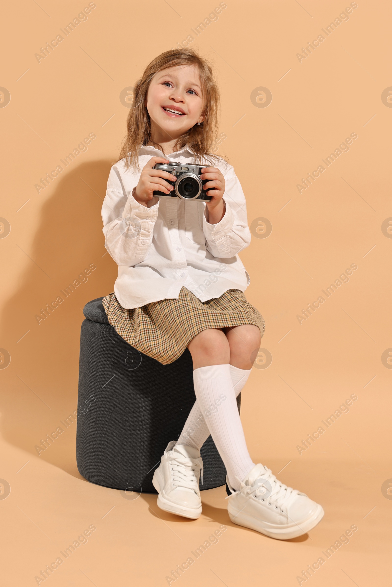 Photo of Fashion concept. Stylish girl with vintage camera on pale orange background