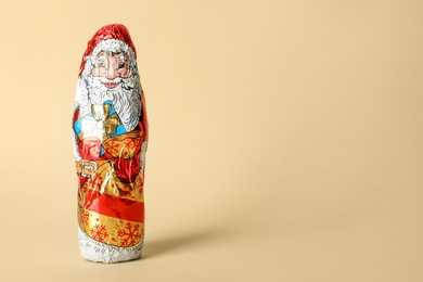 Photo of Chocolate Santa Claus in foil wrapper on beige background. Space for text