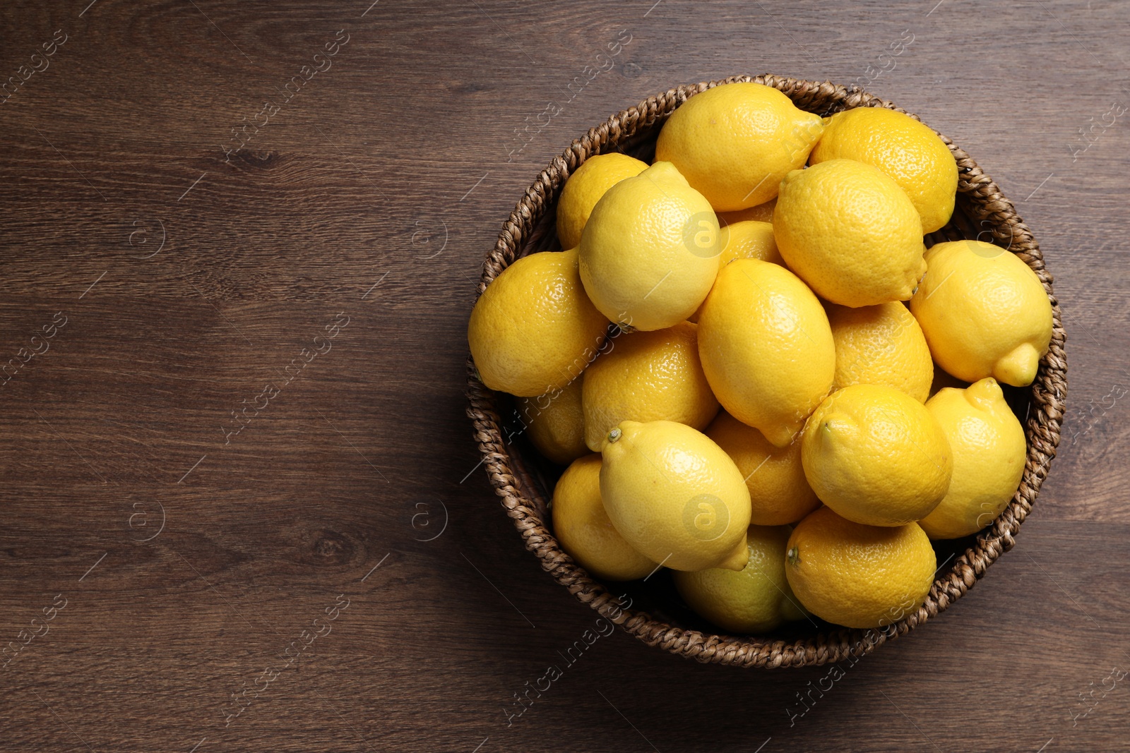 Photo of Fresh lemons in wicker basket on wooden table, top view. Space for text