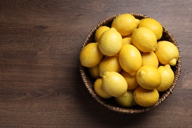 Photo of Fresh lemons in wicker basket on wooden table, top view. Space for text