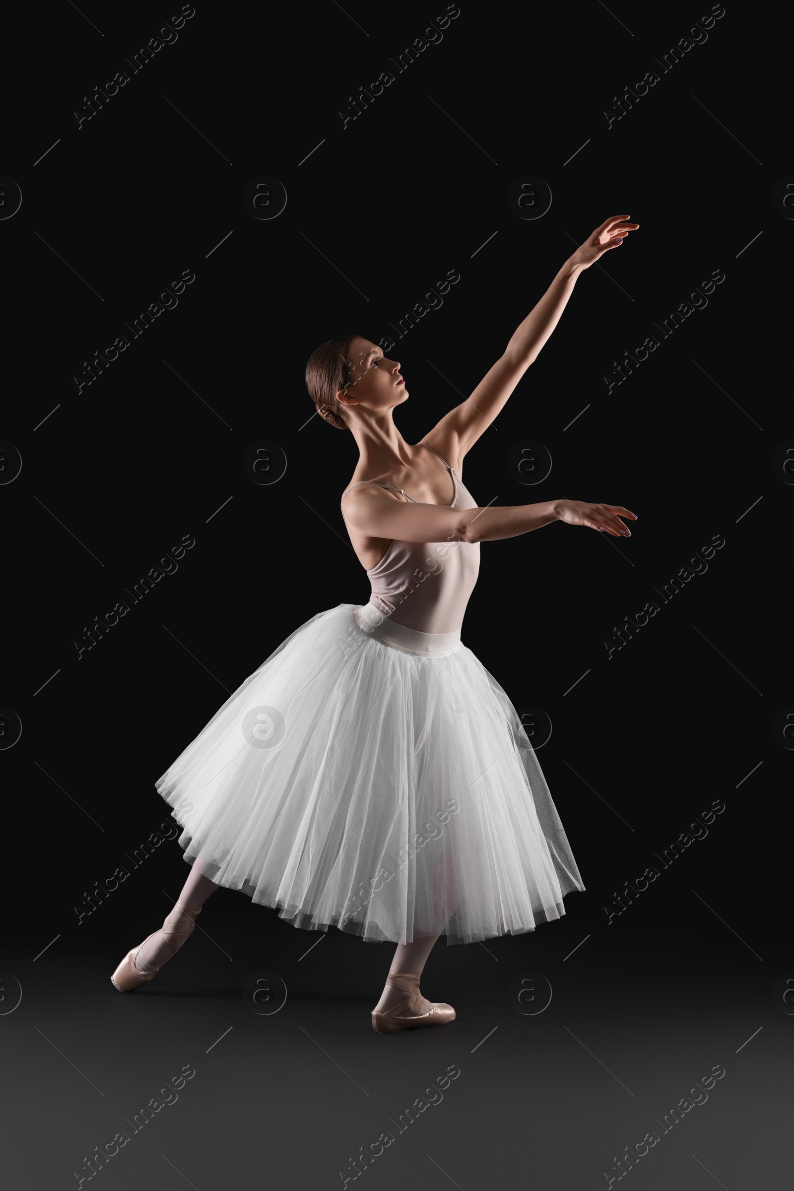 Photo of Young ballerina practicing dance moves on black background