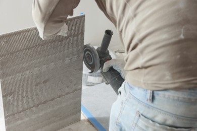 Photo of Worker cutting tile with circular saw indoors, closeup