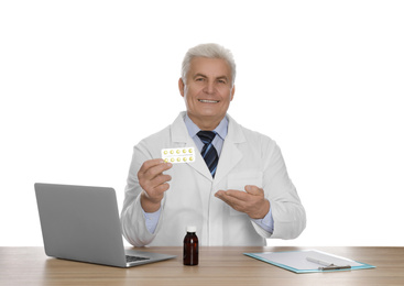 Photo of Professional pharmacist with pills and laptop at table against white background