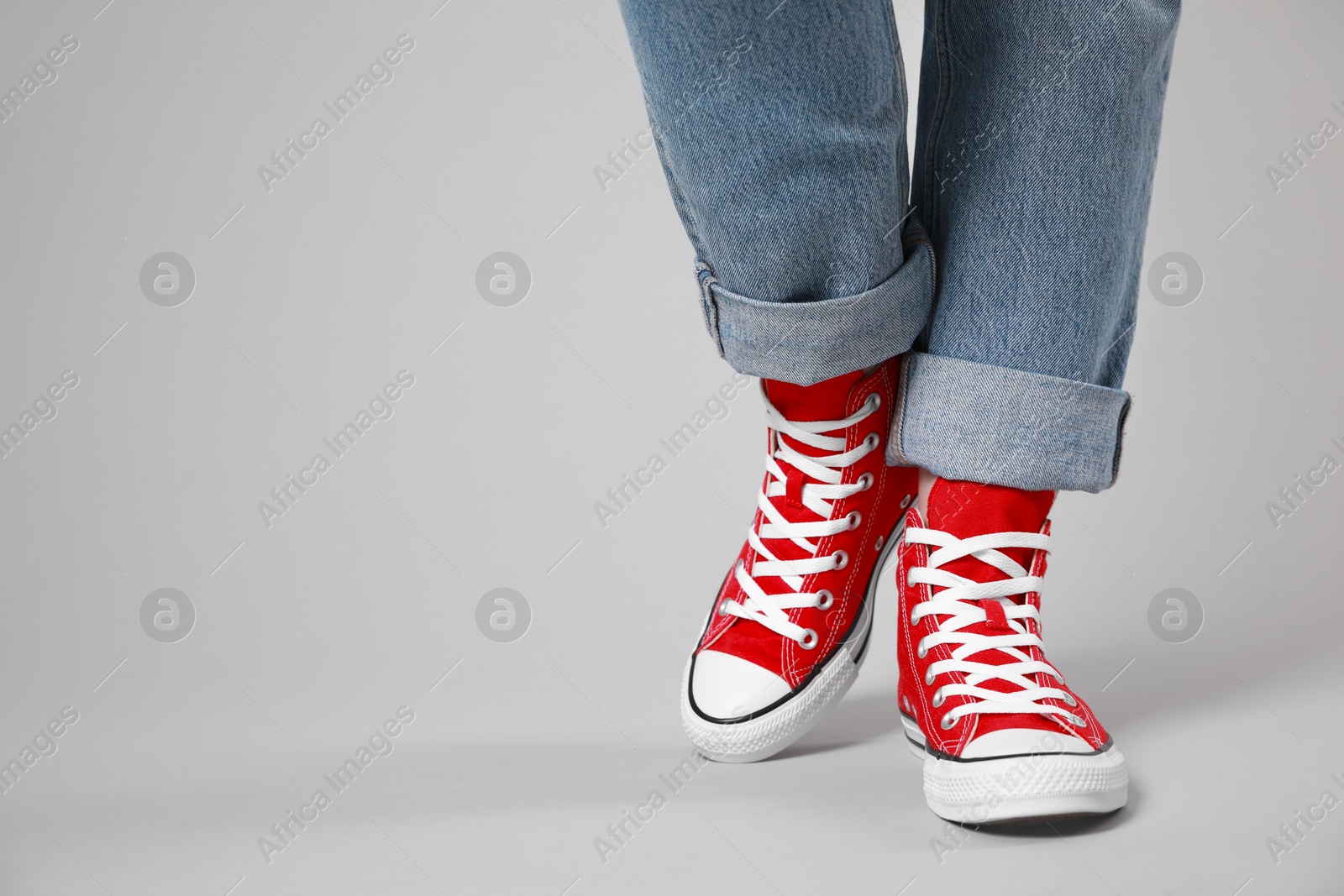 Photo of Woman wearing pair of new stylish sneakers on light grey background, closeup. Space for text