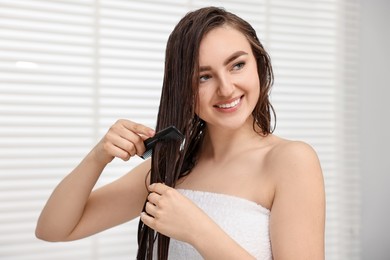 Young woman brushing hair after applying mask indoors