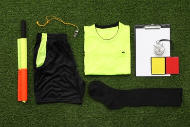 Uniform and other referee equipment on green grass, flat lay