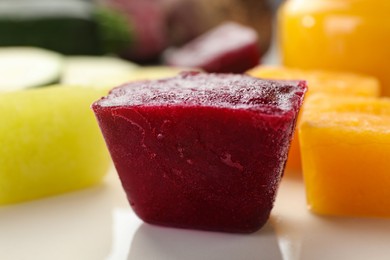 Photo of Frozen beet, pumpkin and zucchini puree cubes on plate, closeup