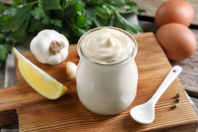 Photo of Fresh mayonnaise sauce in glass jar and ingredients on wooden table, closeup