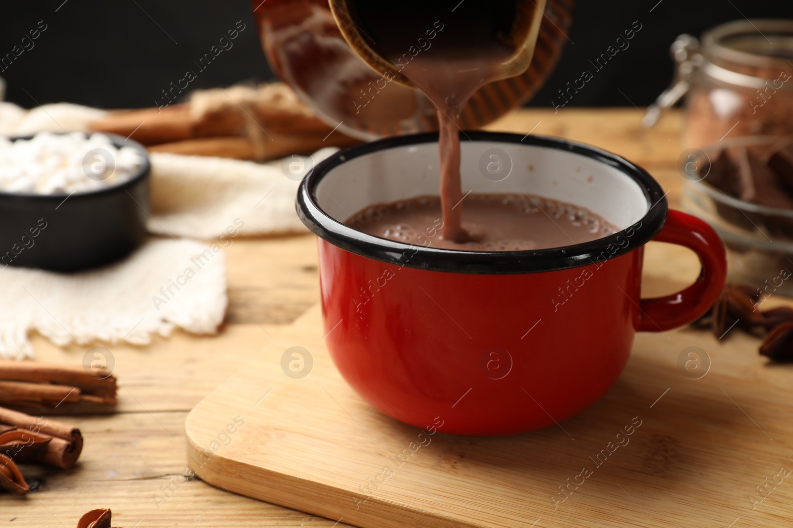 Photo of Pouring tasty hot chocolate into cup at wooden table, closeup