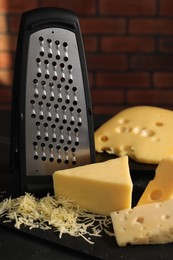 Photo of Grated, cut cheese and grater on black table, closeup