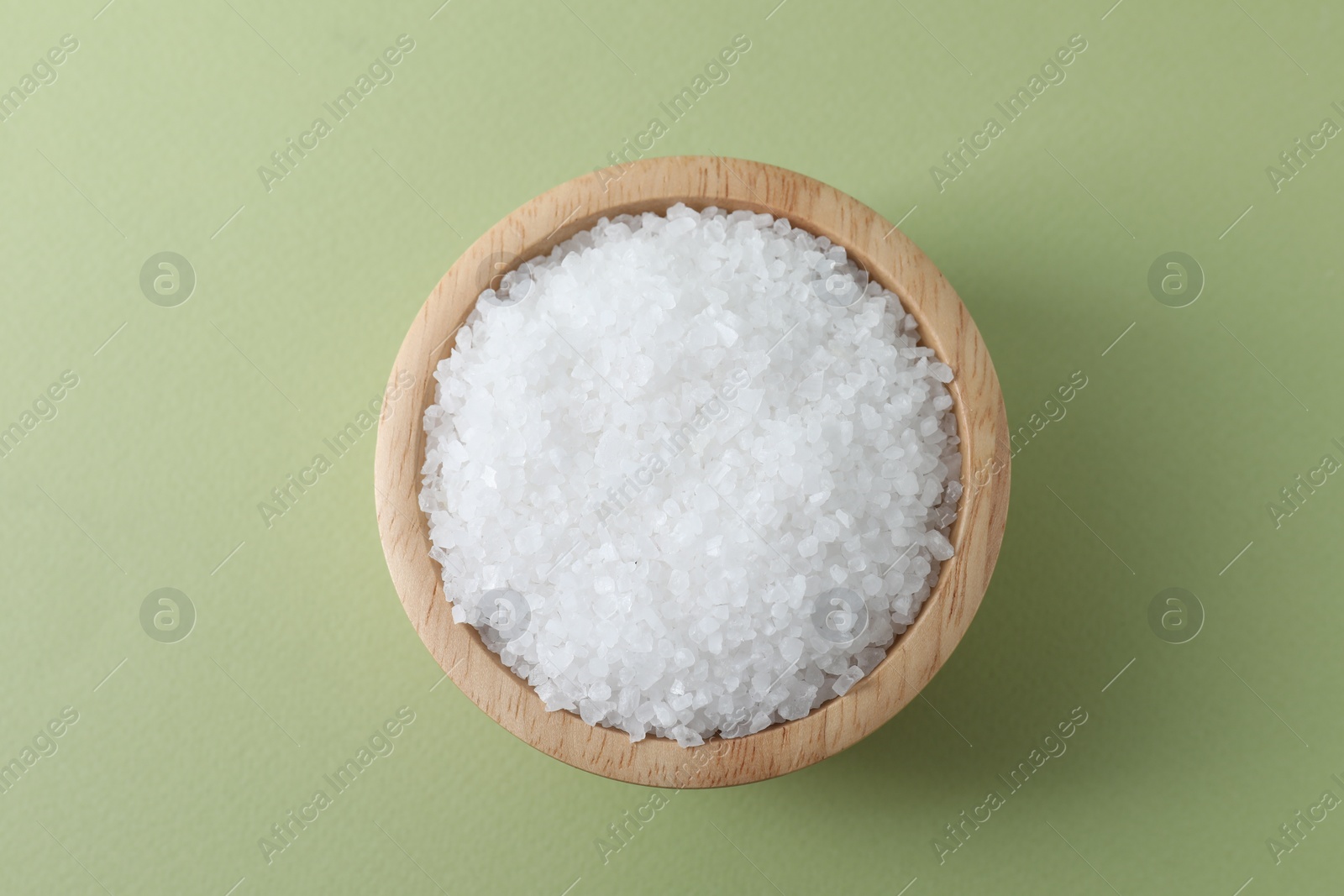 Photo of Organic white salt in bowl on olive background, top view