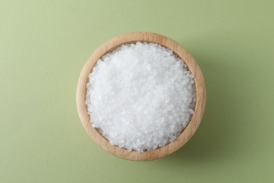 Organic white salt in bowl on olive background, top view