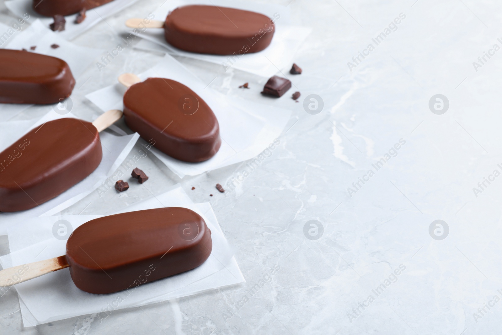 Photo of Glazed ice cream bars and chocolate chunks on light grey table. Space for text