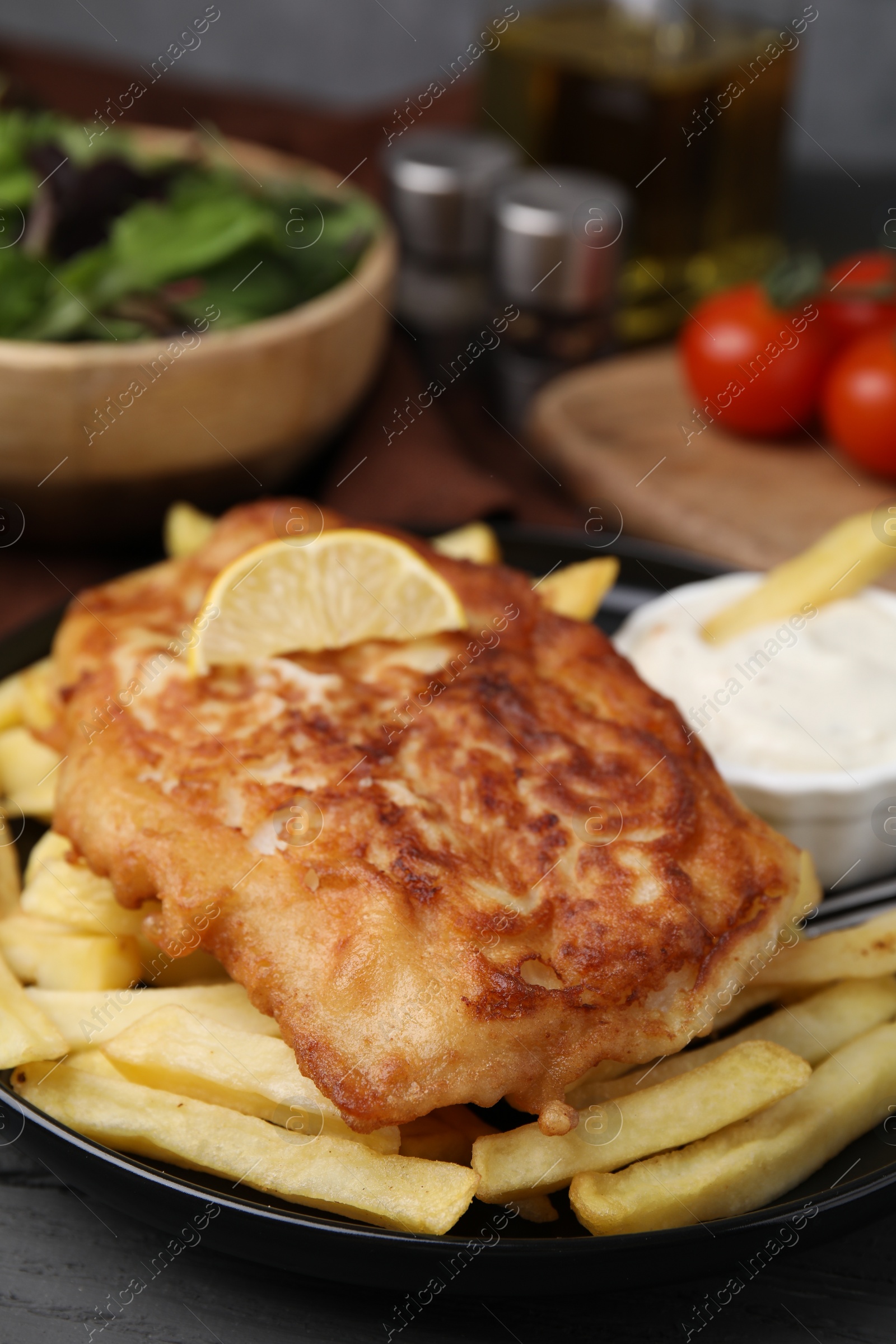 Photo of Tasty soda water battered fish, lemon slice and potato chips on dark wooden table, closeup