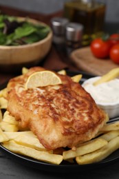Photo of Tasty soda water battered fish, lemon slice and potato chips on dark wooden table, closeup
