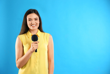 Young female journalist with microphone on blue background. Space for text