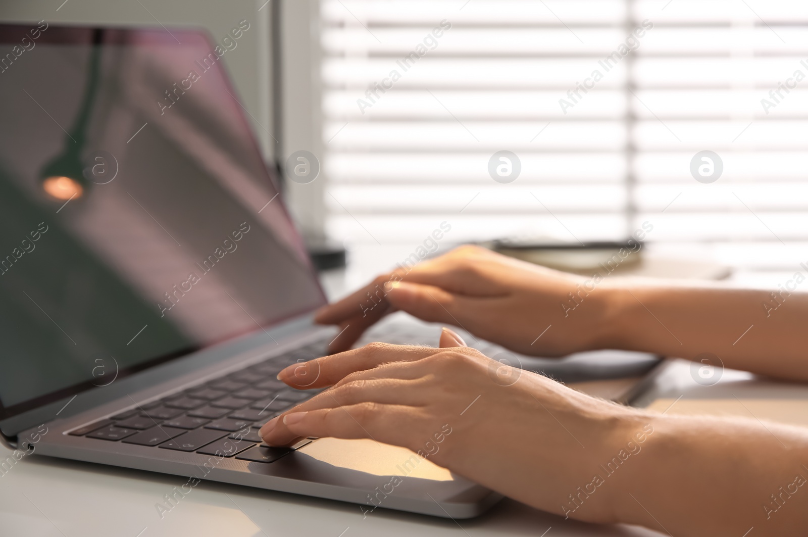 Photo of Woman working with modern laptop at white table, closeup