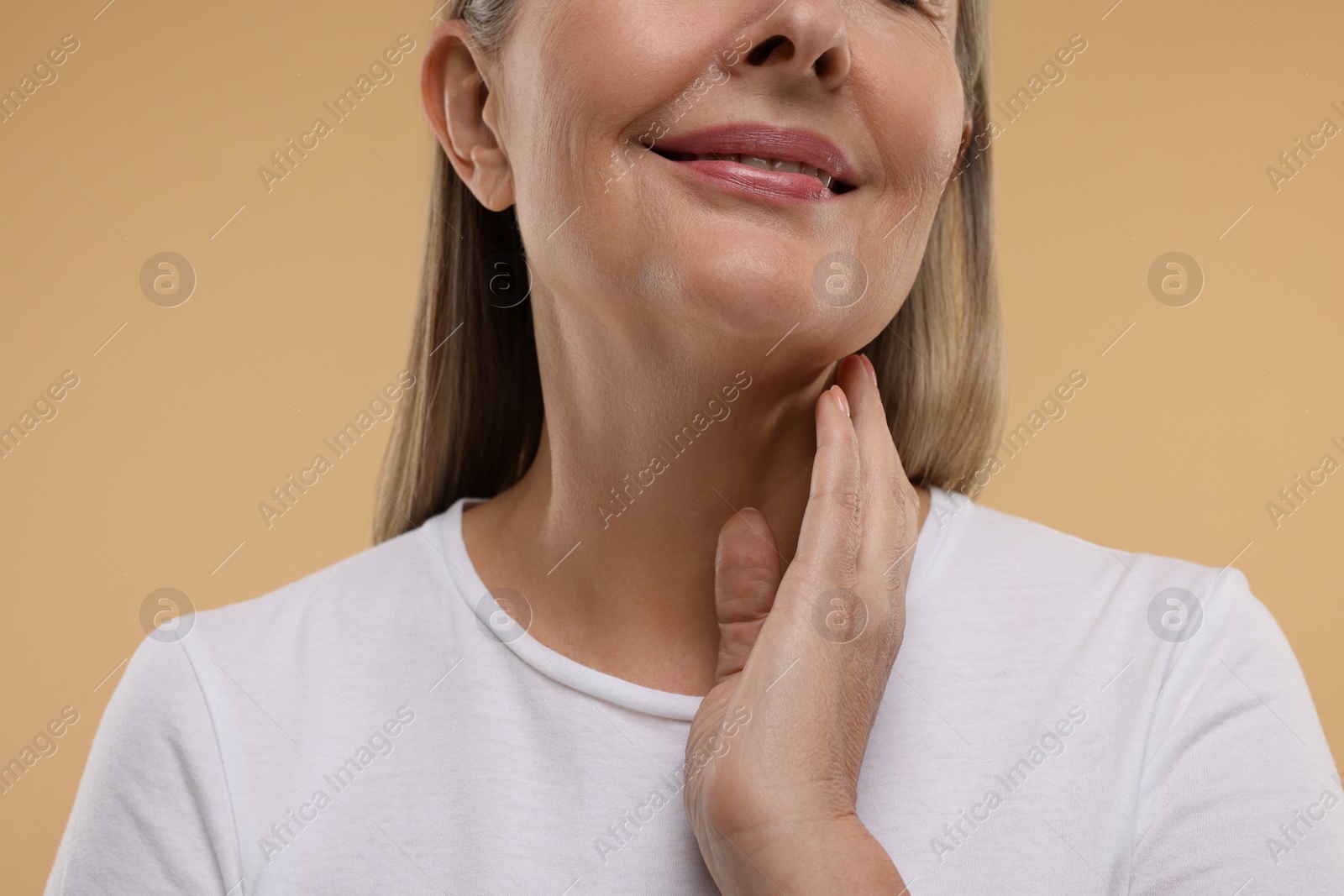 Photo of Mature woman touching her neck on beige background, closeup