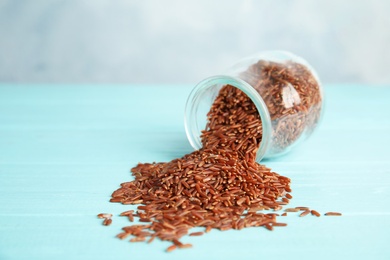 Photo of Jar with uncooked red rice on blue wooden table. Space for text