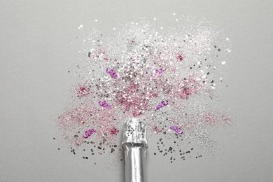 Bottle of champagne for celebration with glitter and confetti on grey background, top view