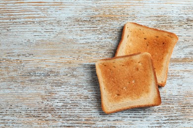 Photo of Slices of delicious toasted bread on wooden table, top view. Space for text