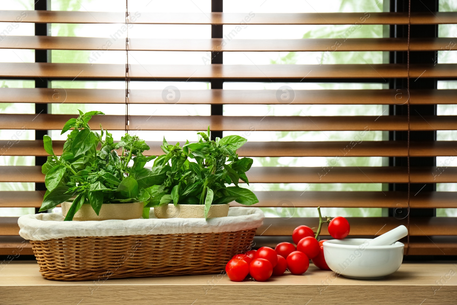 Photo of Green basil, tomatoes and mortar with pestle on window sill indoors