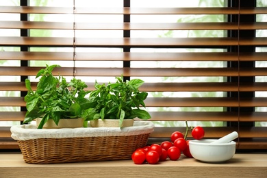 Photo of Green basil, tomatoes and mortar with pestle on window sill indoors