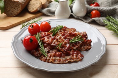 Photo of Slices of tasty fried bacon with rosemary and tomatoes served on wooden table