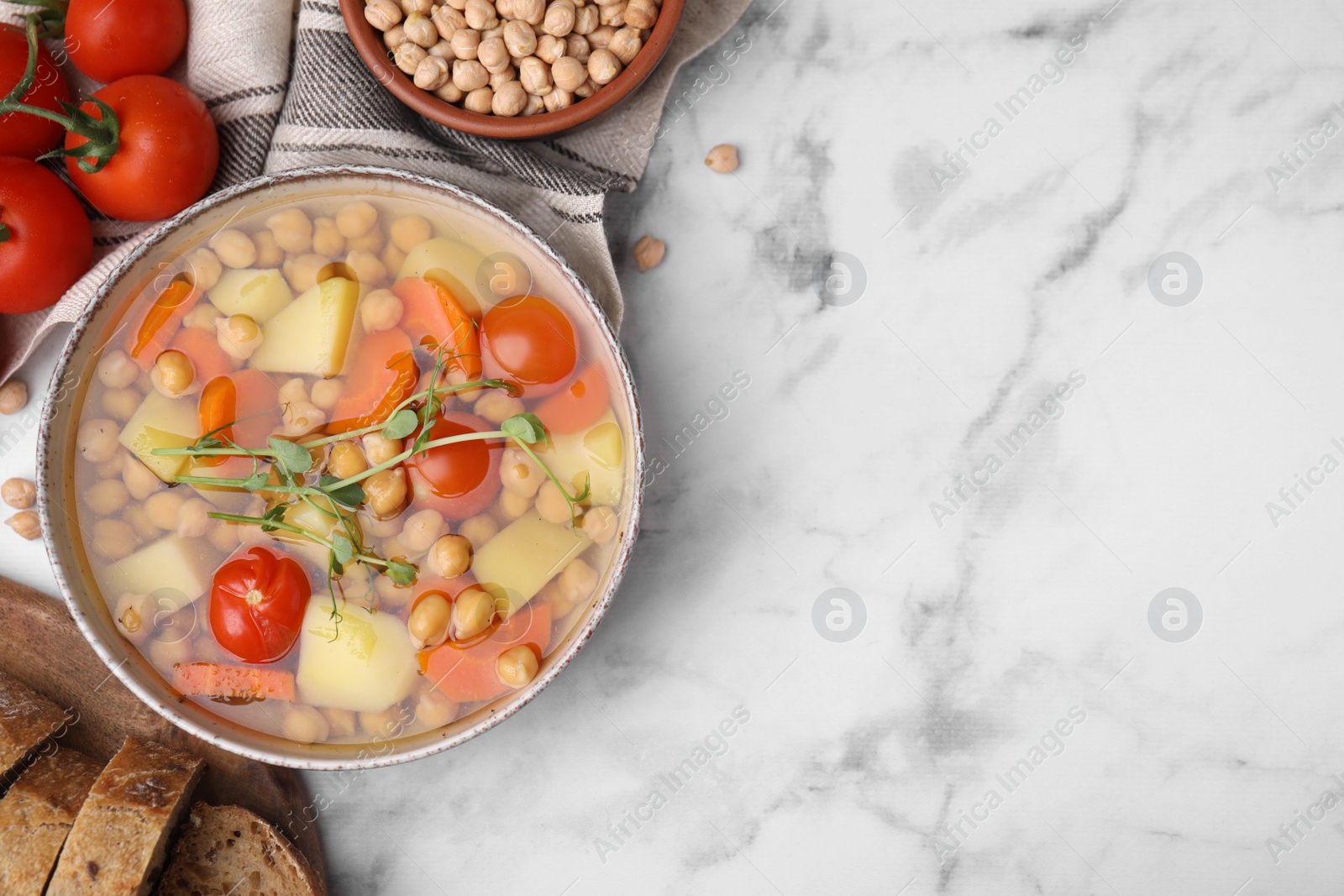 Photo of Tasty chickpea soup in bowl and ingredients served on white marble table, flat lay. Space for text