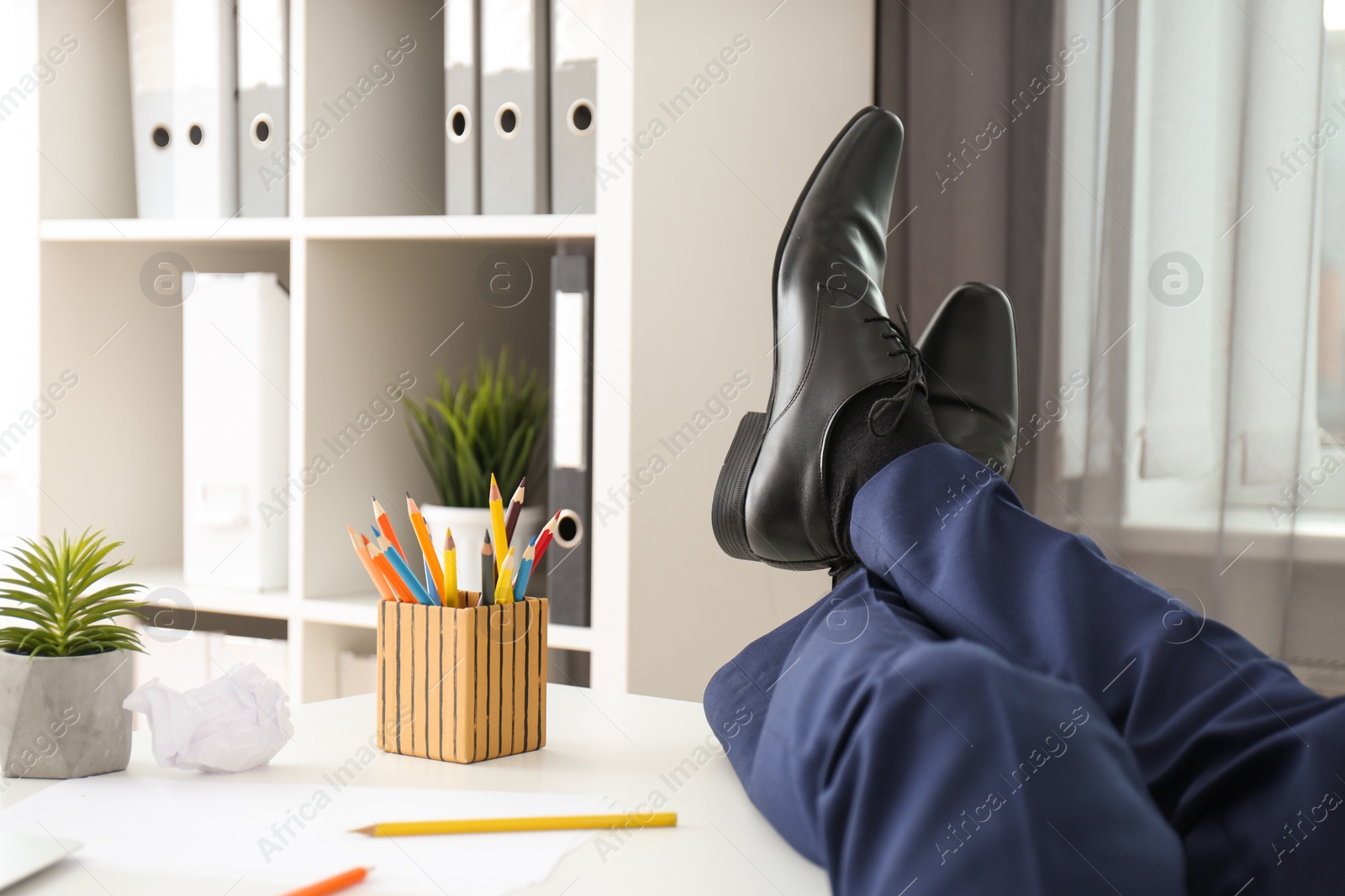 Photo of Lazy young man resting with feet on desk in office, closeup