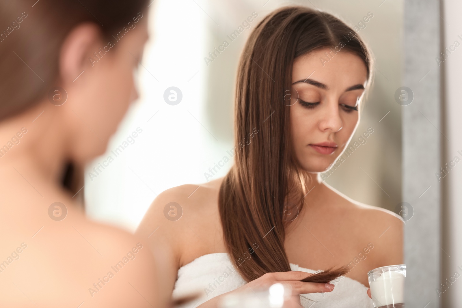 Photo of Woman with glass bowl of hair mask in front of mirror indoors