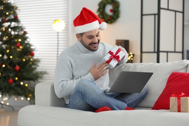 Photo of Celebrating Christmas online with exchanged by mail presents. Man with gift box during video call on laptop at home