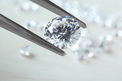 Photo of Tweezers with beautiful shiny diamond against light blurred background, closeup