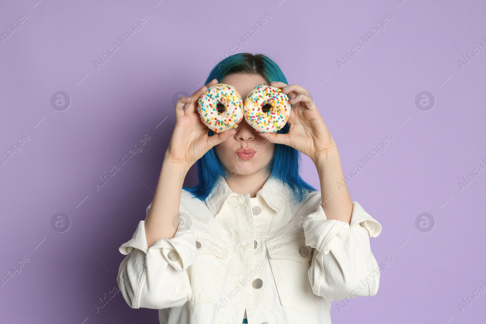 Photo of Young woman with bright dyed hair holding donuts on lilac background