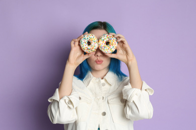 Young woman with bright dyed hair holding donuts on lilac background