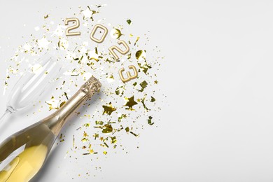 Photo of Bottle of sparkling wine, glass, golden confetti and number 2023 on white background, flat lay with space for text. Happy New Year