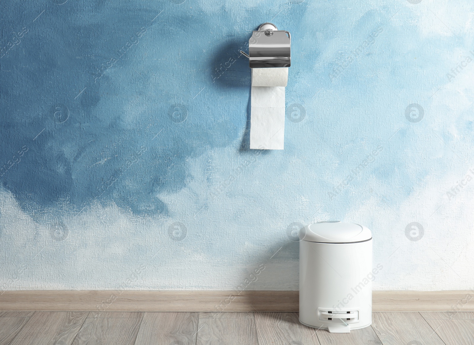 Photo of Toilet paper holder with roll and trash bin near color wall. Space for text