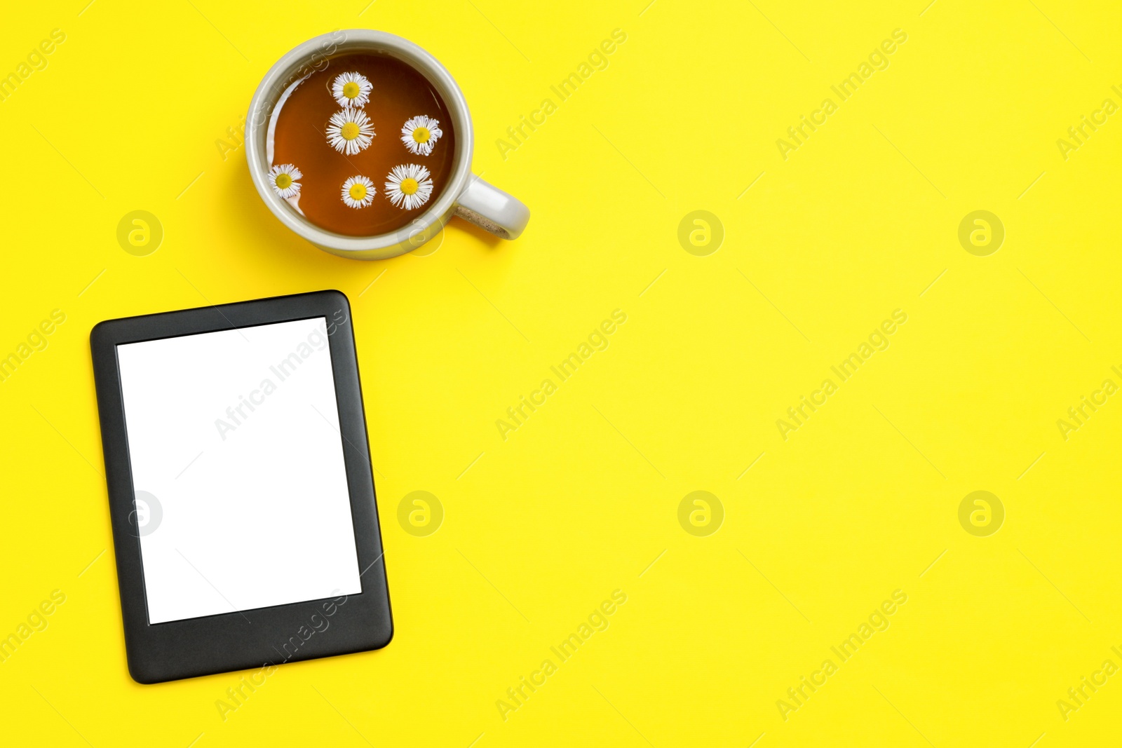 Photo of Modern e-book reader and cup of chamomile tea on yellow background, flat lay. Space for text