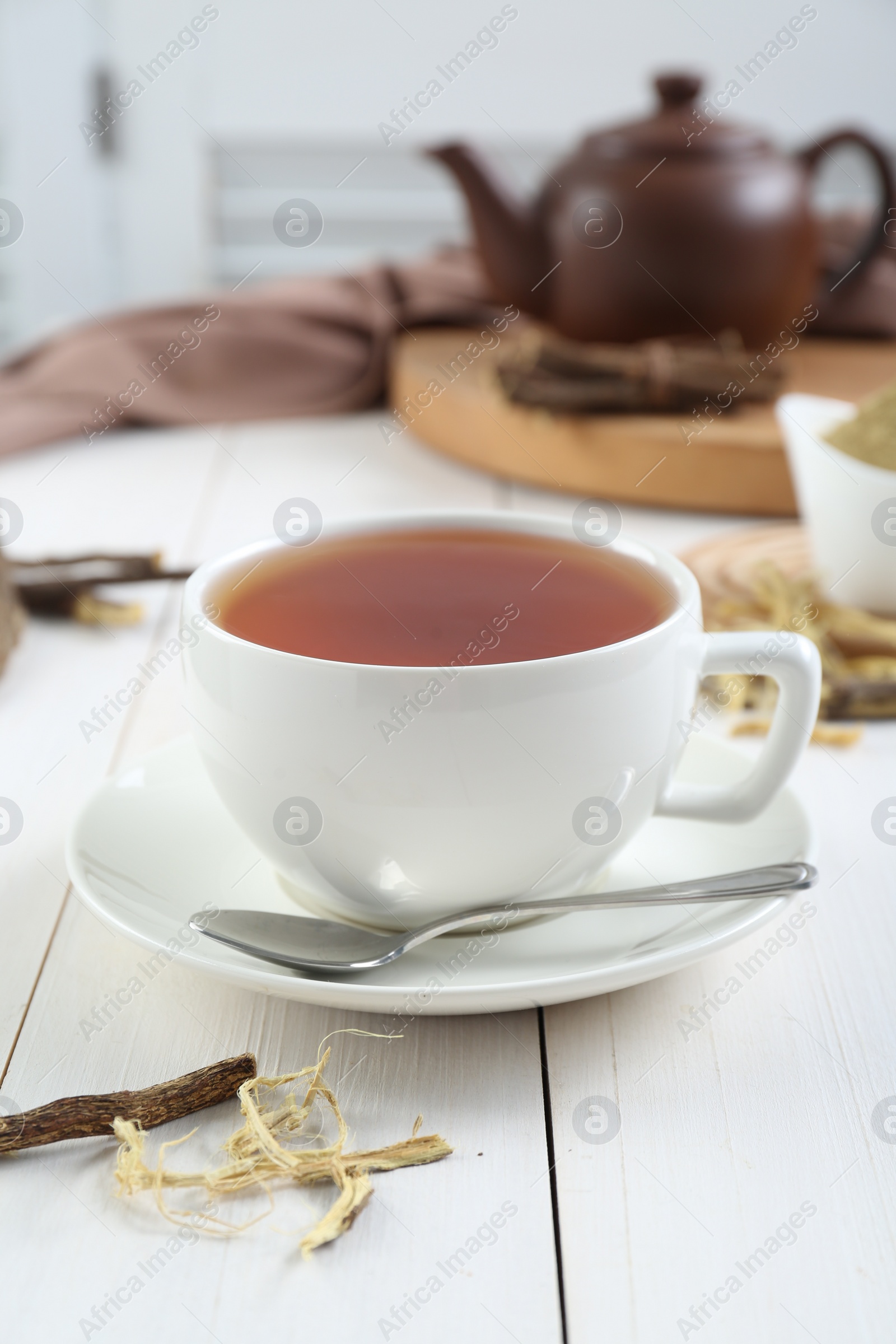 Photo of Aromatic licorice tea in cup and dried sticks of licorice root on white wooden table