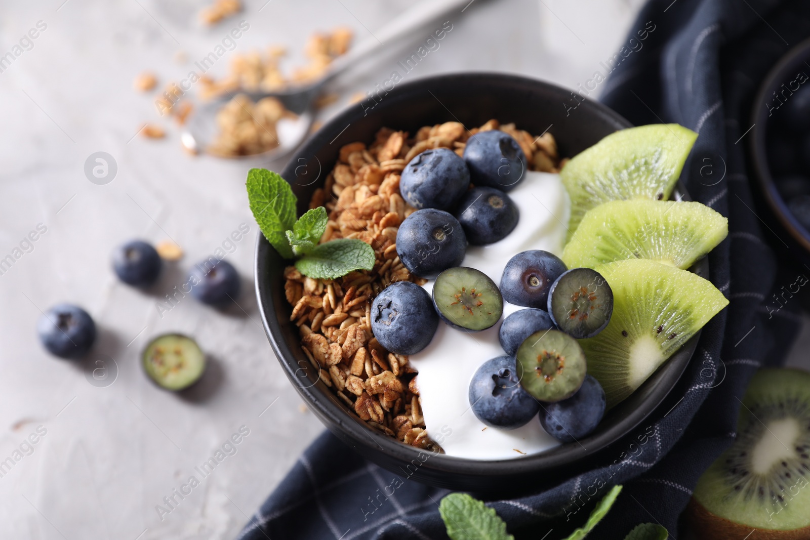 Photo of Tasty granola with yogurt, blueberries and kiwi in bowl on gray table, closeup