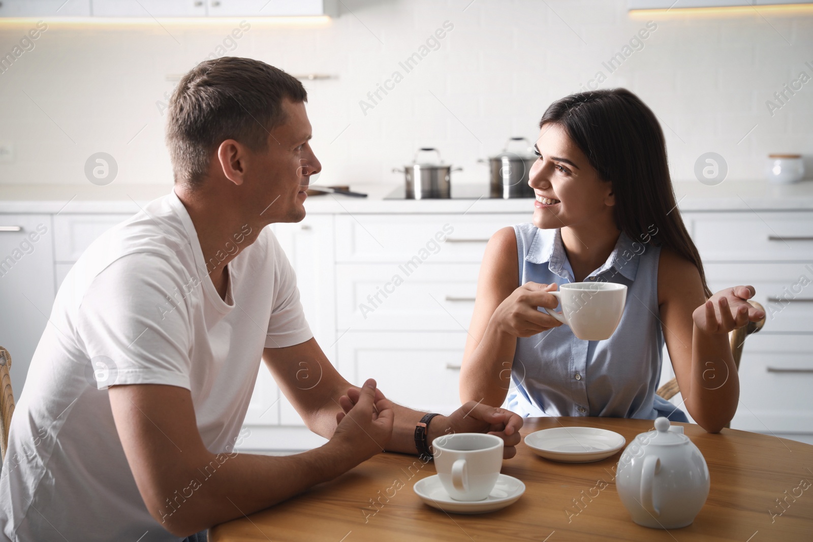 Photo of Man and woman talking while drinking tea at table in kitchen