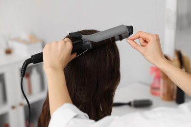 Photo of Hairdresser working with client using curling hair iron in salon, closeup