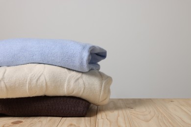 Stack of casual sweaters on wooden table against light grey background. Space for text